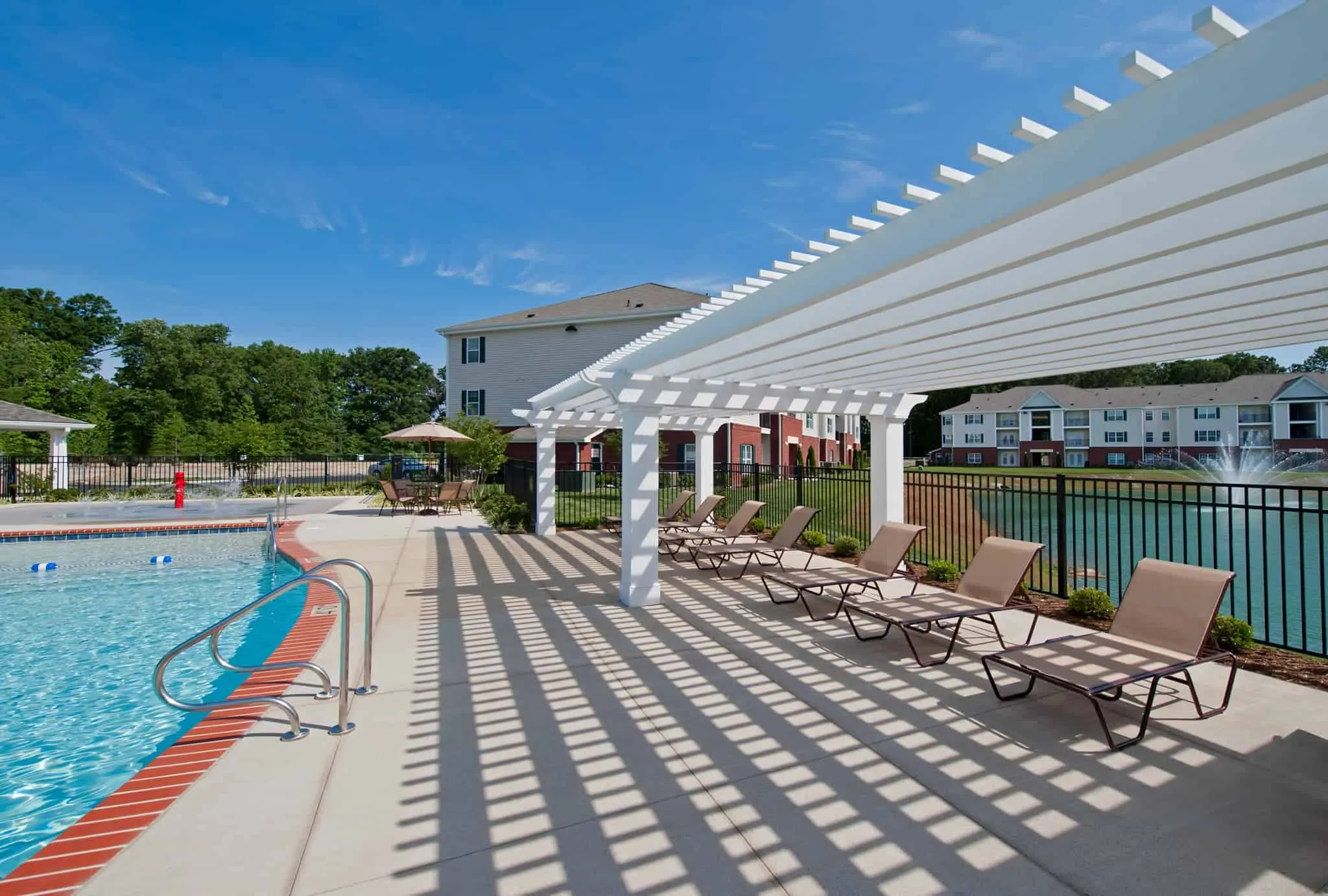 A sun-drenched pool deck featuring several lounge chairs positioned under the shade of a white pergola A sun-drenched pool deck featuring several lounge chairs positioned under the shade of a white pergola